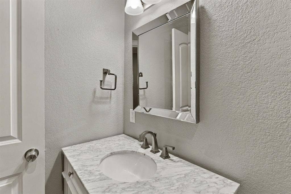 510 E Malone Street, Celina, TX 75009 Vanity featuring a stone-surface countertop, integrated oval basin, polished metal widespread faucet, framed beveled-edge wall mirror, and dual-light fixture