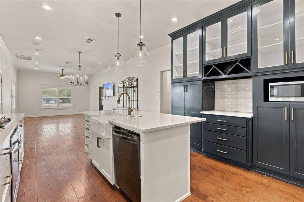 510 E Malone Street, Celina, TX 75009 Kitchen featuring floor-to-ceiling dark cabinetry with glass-front uppers, a central island with a farmhouse sink, white stone countertops, subway tile backsplash, and wood-finish flooring