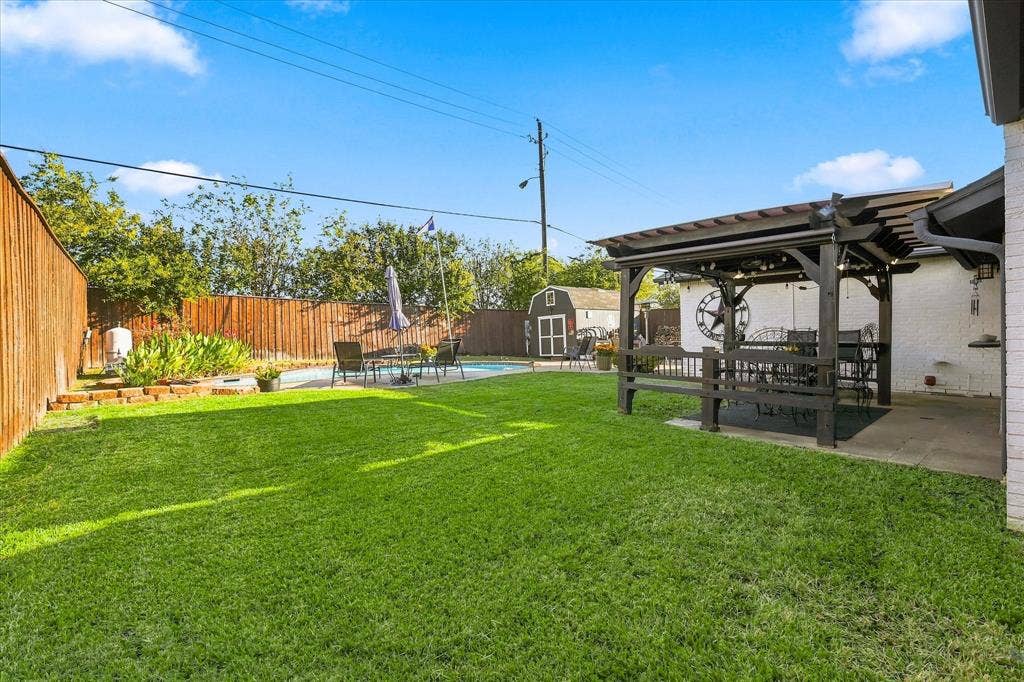 2117 Northmoor Drive, Carrollton, TX 75006 Private backyard featuring a swimming pool, covered wooden pergola, wood privacy fencing, and a detached storage structure