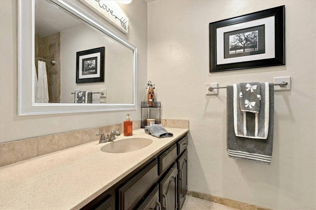 2117 Northmoor Drive, Carrollton, TX 75006 Wall-mounted mirror with a white frame, single-basin vanity with a stone-composite countertop, and stone-tile backsplash