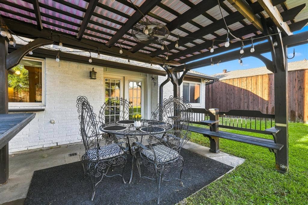 2117 Northmoor Drive, Carrollton, TX 75006 Covered patio featuring a timber pergola, built-in wooden bench seating, concrete flooring, and exterior wall-mounted lighting