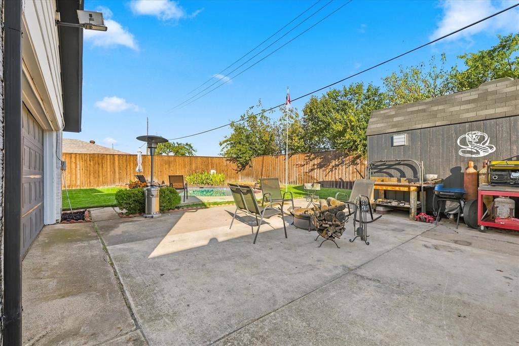 2117 Northmoor Drive, Carrollton, TX 75006 Backyard featuring a concrete patio, inground pool, wood perimeter fencing, and a detached storage structure
