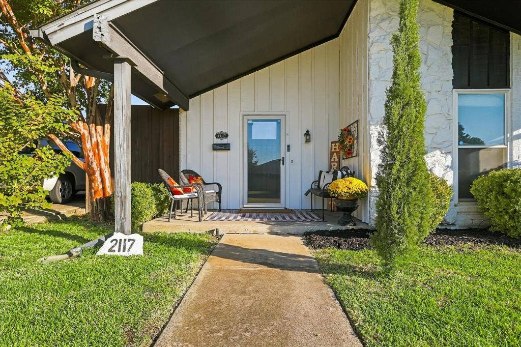 2117 Northmoor Drive, Carrollton, TX 75006 Covered front entryway featuring vertical siding, stone masonry accents, a concrete walkway, and an attached porch overhang