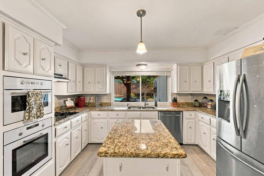 2117 Northmoor Drive, Carrollton, TX 75006 Kitchen featuring white cabinetry, stone countertops, a central island, stainless steel appliances, and wood-finish flooring