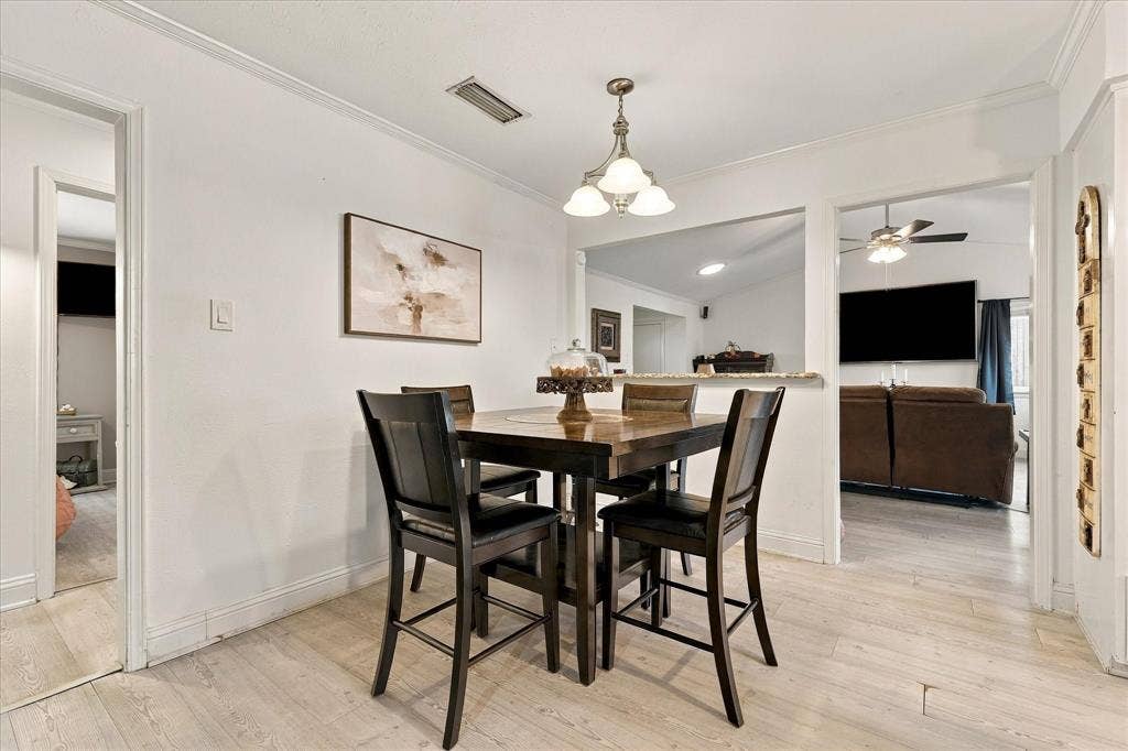 2117 Northmoor Drive, Carrollton, TX 75006 Dining area featuring light-toned wood-finish flooring, a multi-light pendant fixture, and a pass-through wall opening with a stone-top counter