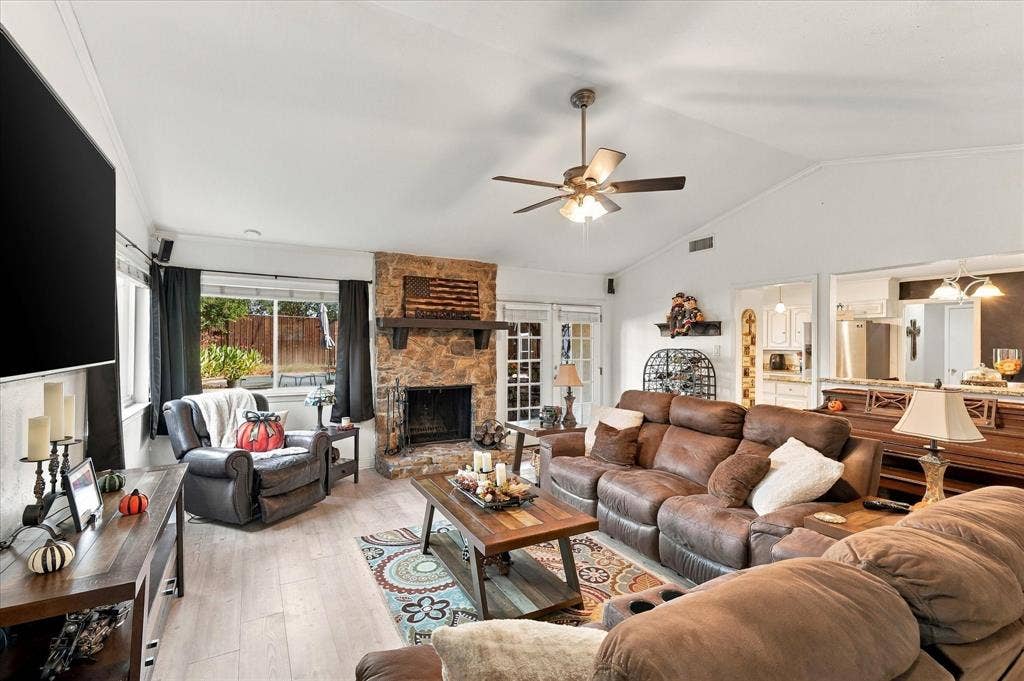 2117 Northmoor Drive, Carrollton, TX 75006 Vaulted ceiling, stone-faced fireplace with a wood mantel, wood-finish flooring, and a ceiling fan with integrated lighting