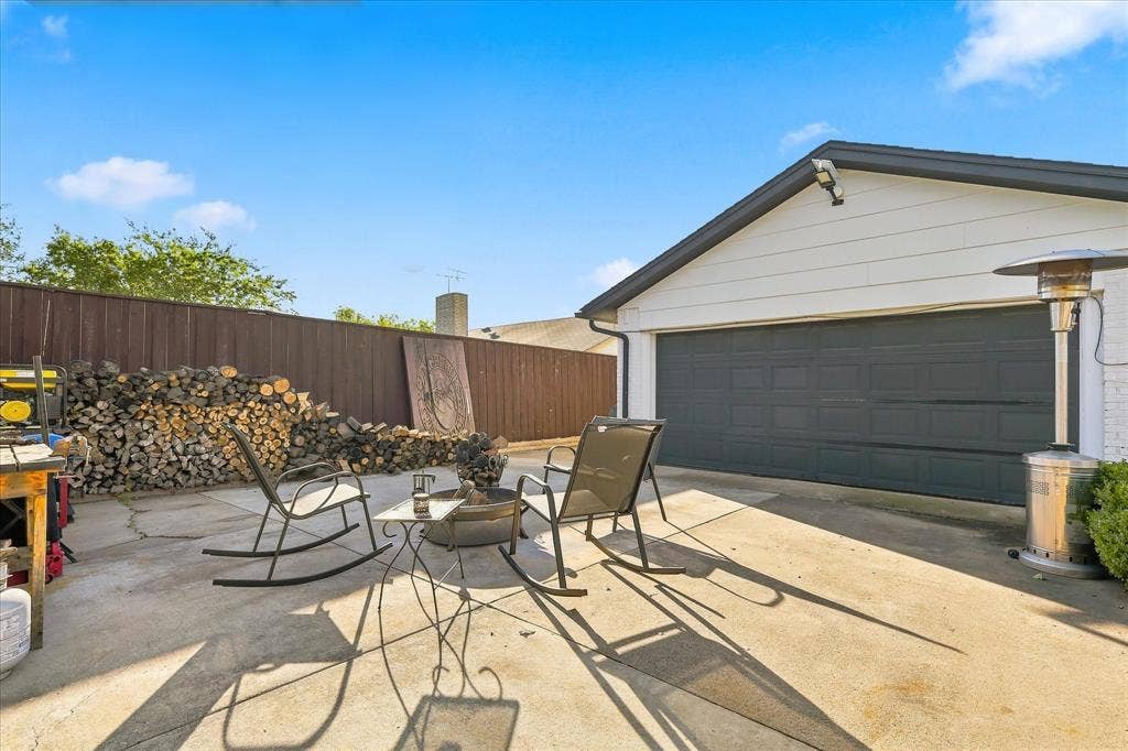 2117 Northmoor Drive, Carrollton, TX 75006 Concrete patio area featuring a detached garage with a paneled door and enclosed by wood fencing