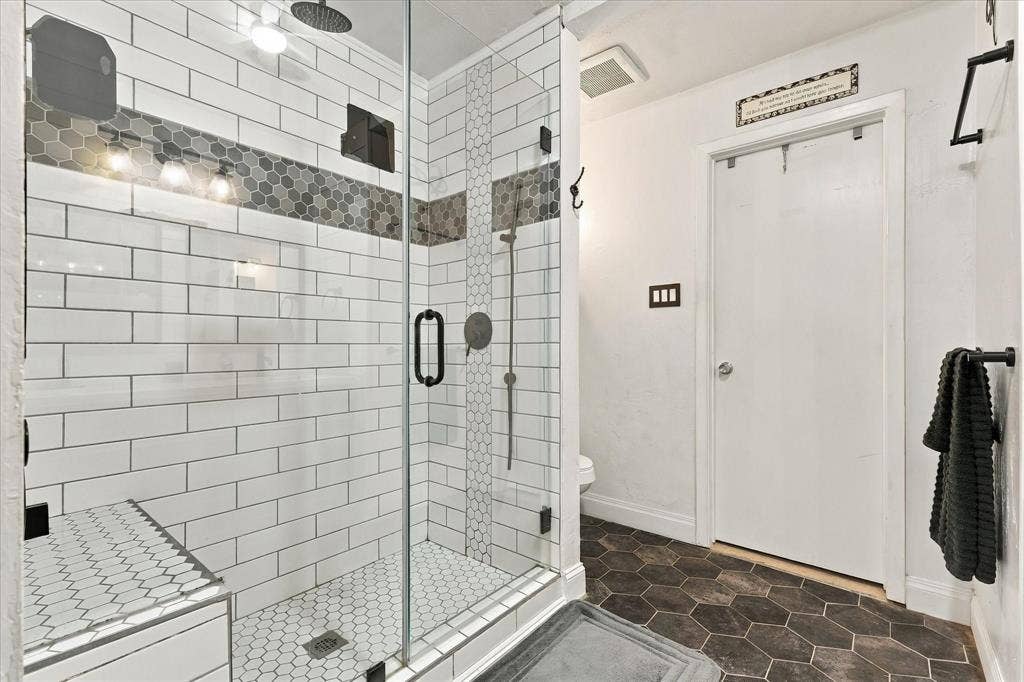 2117 Northmoor Drive, Carrollton, TX 75006 Walk-in shower featuring a glass enclosure, rainfall showerhead, white subway tile walls, and decorative hexagonal tile accents with a coordinating hexagonal floor tile