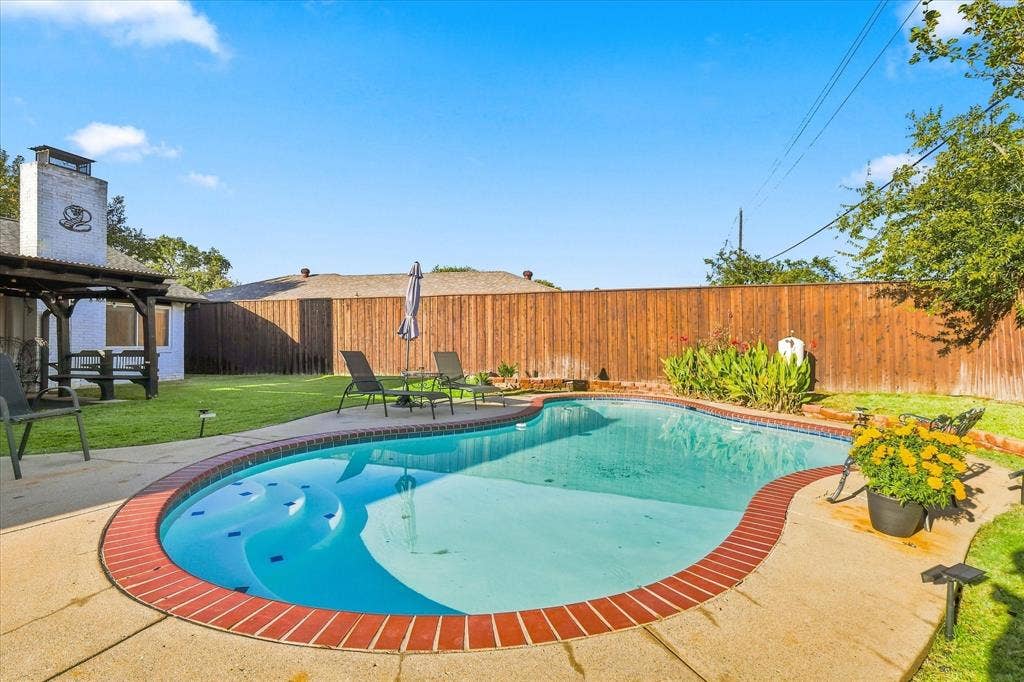2117 Northmoor Drive, Carrollton, TX 75006 Backyard featuring an in-ground swimming pool with brick coping, concrete patio, covered patio structure, and perimeter wood privacy fencing
