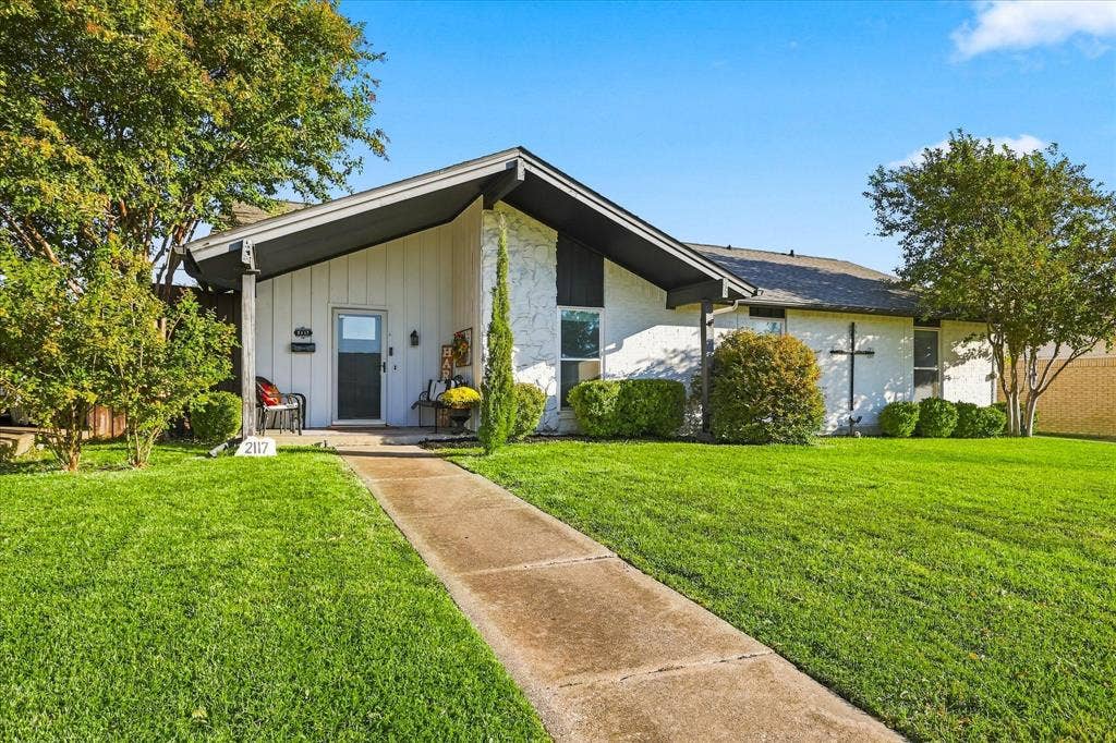 2117 Northmoor Drive, Carrollton, TX 75006 Mid-century modern architectural style featuring a low-pitched gable roof, board-and-batten siding, textured masonry facade, and an elongated concrete walkway