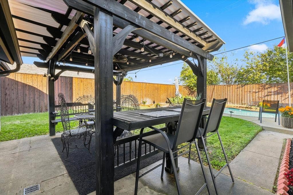 2117 Northmoor Drive, Carrollton, TX 75006 Outdoor living space featuring a wood-frame pergola, concrete patio, swimming pool, and wood privacy fencing