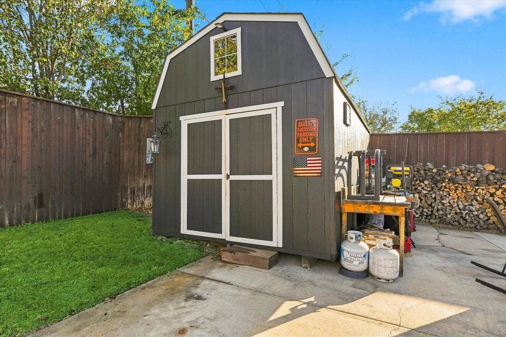 2117 Northmoor Drive, Carrollton, TX 75006 Detached storage structure featuring a gambrel roofline, vertical siding, double-door entry, and a windowed loft gable