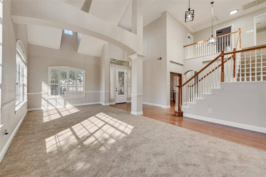 2017 Lunenburg Drive, Allen, TX 75013 High-ceiling interior featuring arched architectural columns, a staircase with a wooden handrail and balusters, wood-finish flooring, and arched window detailing