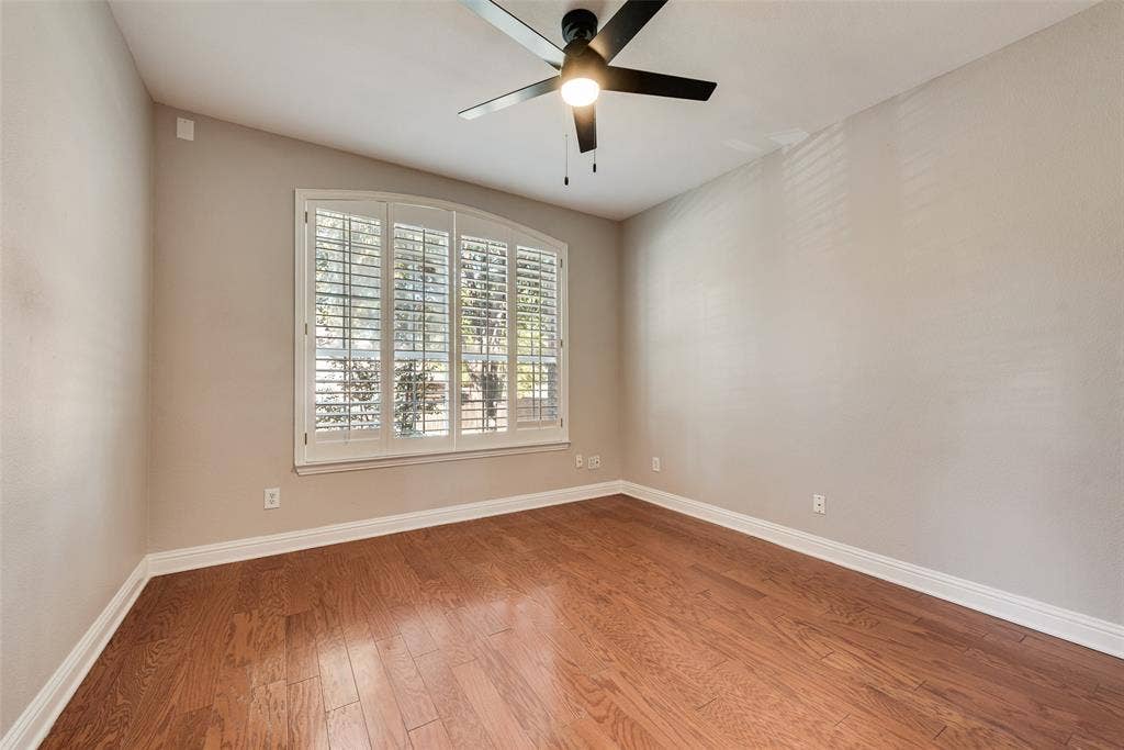 2017 Lunenburg Drive, Allen, TX 75013 Room featuring wood-finish flooring, an arched window with plantation shutters, and a matte black ceiling fan with an integrated light fixture