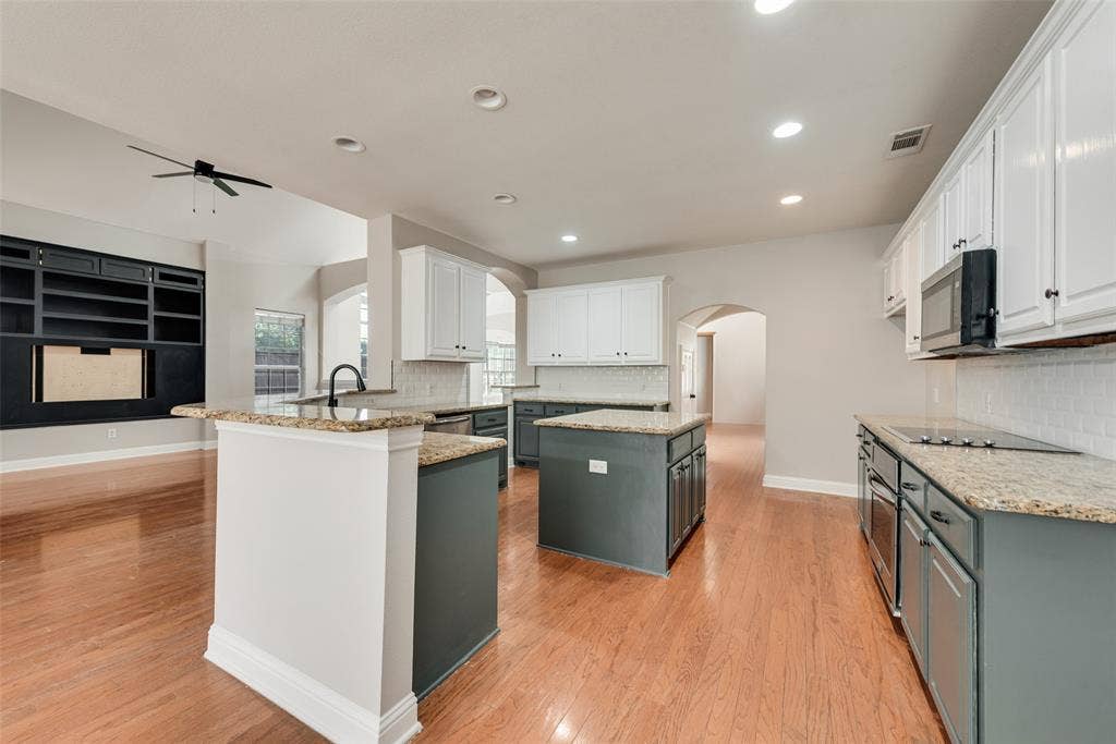 2017 Lunenburg Drive, Allen, TX 75013 Kitchen featuring two-tone cabinetry, stone countertops, subway tile backsplash, built-in black shelving unit, and wood-finish flooring