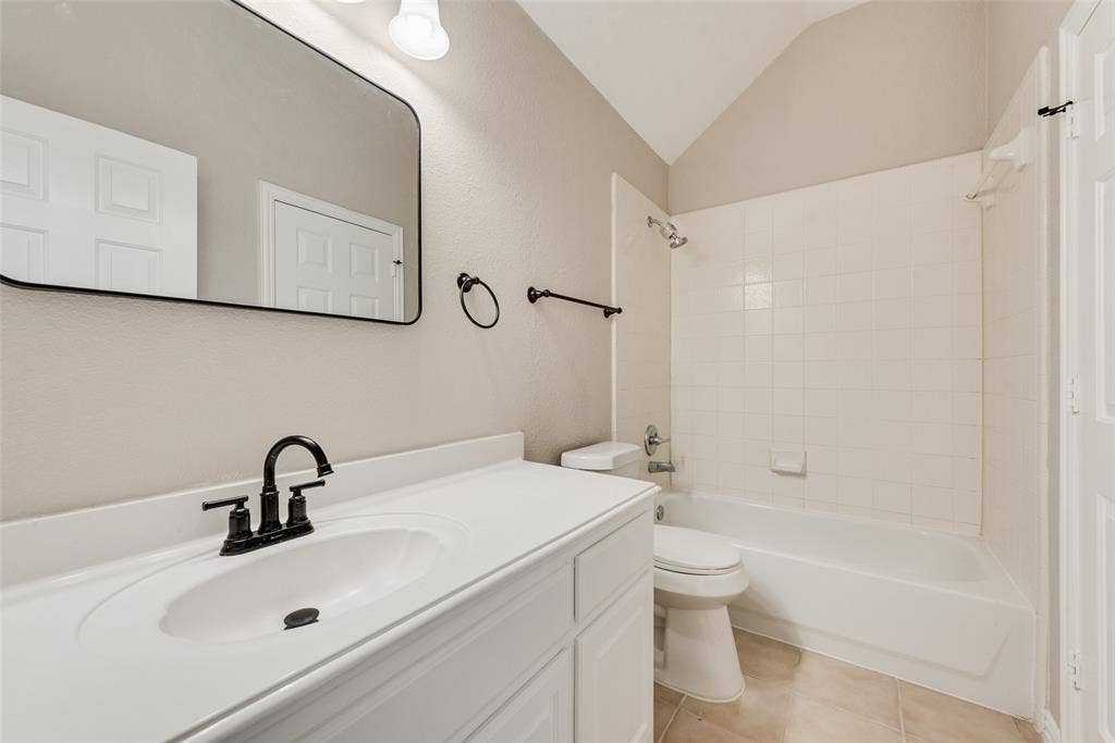 2017 Lunenburg Drive, Allen, TX 75013 Bathroom featuring a vaulted ceiling, vanity with a white countertop and oval undermount sink, matte black faucet, and a shower-tub combination with tile surround