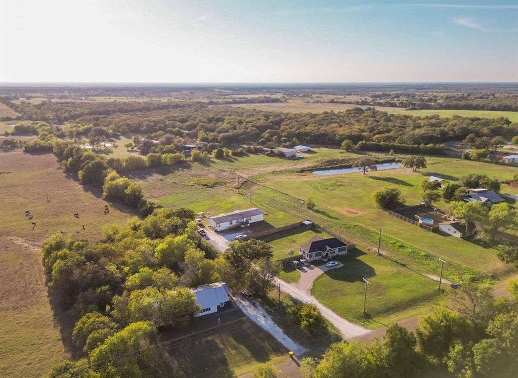 3659 N Katy Road, Ross, TX 76640 Aerial perspective of a sprawling property featuring expansive acreage, mature tree clusters, open pasture land, and a private pond
