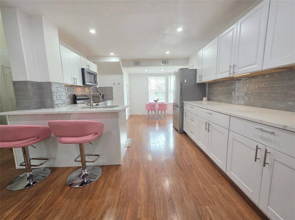 9436 Penny Lane, Irving, TX 75063 Kitchen featuring white shaker-style cabinetry, solid-quartz countertops, grey subway tile backsplash, stainless steel appliances, and wood-finish flooring