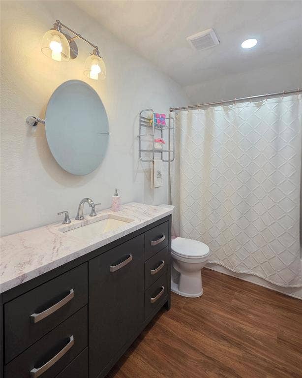 9436 Penny Lane, Irving, TX 75063 Dark charcoal vanity with a stone-finish countertop, integrated sink, polished metal hardware, circular wall mirror, and wood-finish flooring