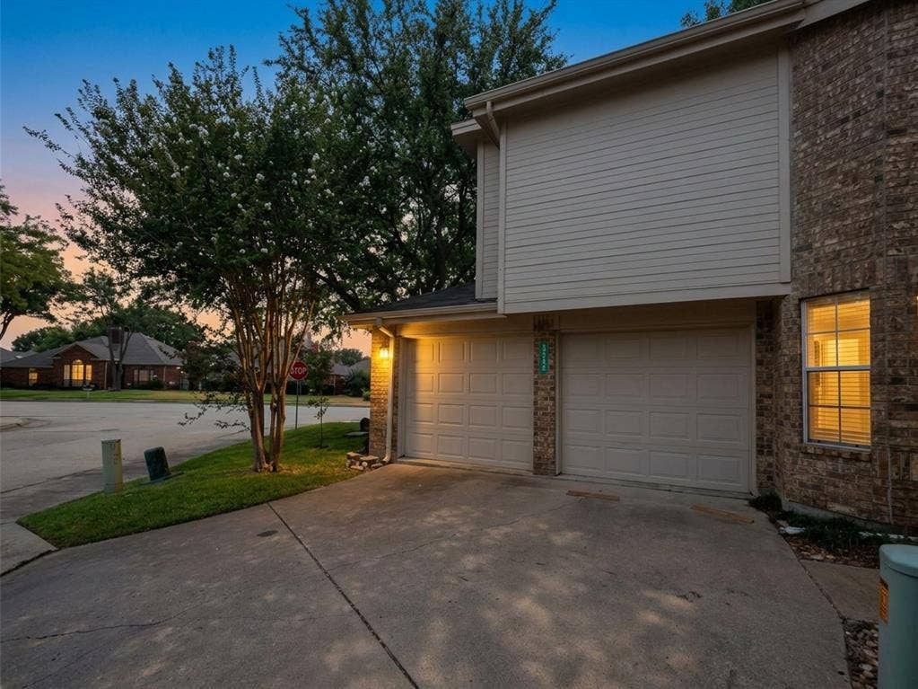 9436 Penny Lane, Irving, TX 75063 Exterior elevation featuring a two-car garage, brick veneer siding, horizontal lap siding, and a concrete driveway