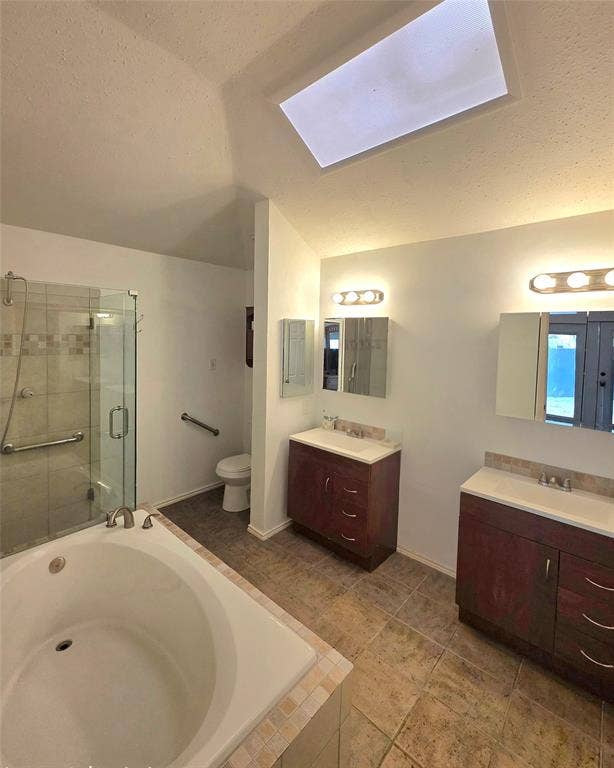 9436 Penny Lane, Irving, TX 75063 Bathroom featuring a soaking tub, glass-enclosed shower, dual wood-finish vanities with rectangular sinks, and a skylight