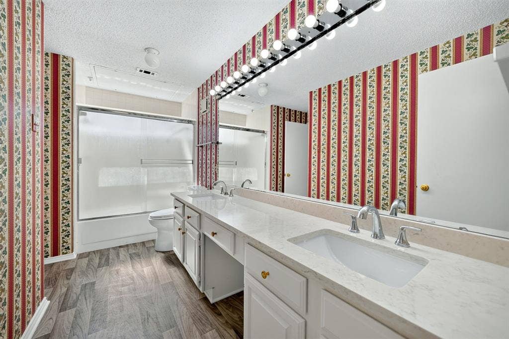 5859 Frankford Road, #1209, Dallas, TX 75252 Dual-sink vanity with a light-toned countertop, wood-finish flooring, full-width wall mirror, and tub-shower combination with sliding glass doors