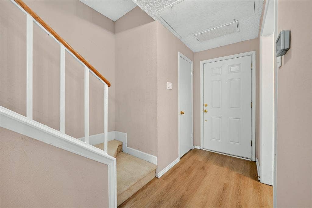 5859 Frankford Road, #1209, Dallas, TX 75252 Entryway featuring wood-finish flooring, a solid-core six-panel door with gold-tone hardware, and a staircase with a white-finished railing and wood-tone handrail