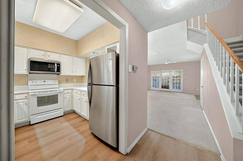 5859 Frankford Road, #1209, Dallas, TX 75252 Kitchen featuring white cabinetry, wood-finish flooring, and stainless steel appliances, paired with an interior staircase boasting a white handrail and wooden banister