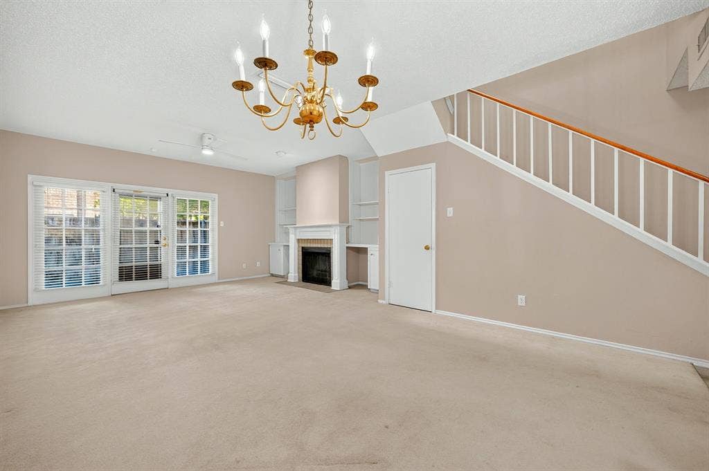 5859 Frankford Road, #1209, Dallas, TX 75252 Fireplace with detailed mantel, built-in shelving, glass-paned sliding doors, tiered chandelier, and staircase with wooden handrail