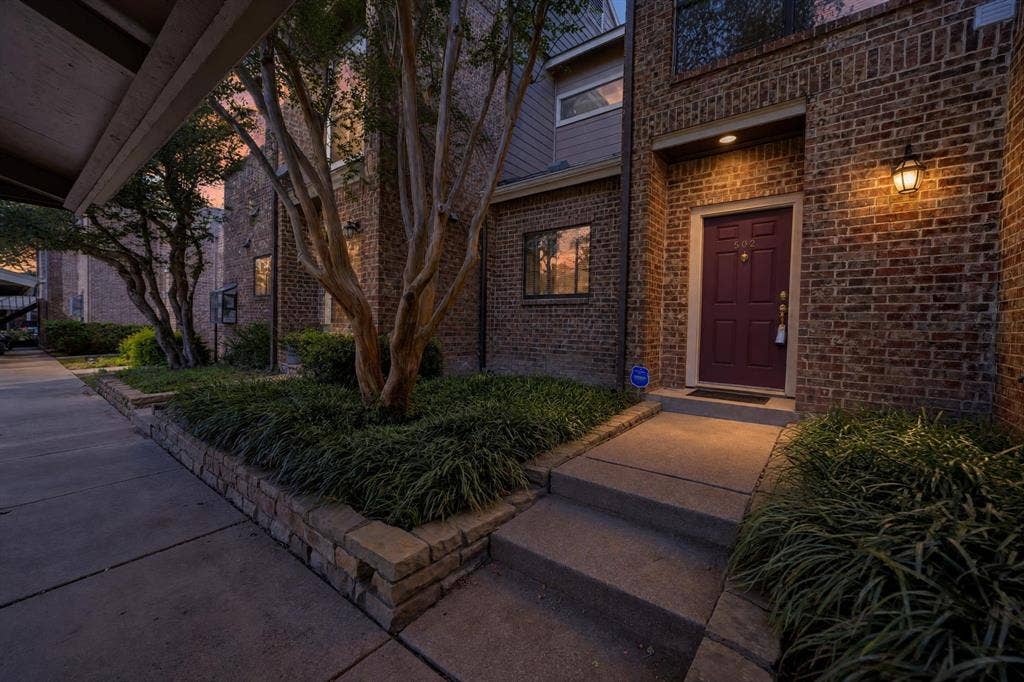 5859 Frankford Road, #1209, Dallas, TX 75252 Brick exterior featuring a recessed entry, concrete walkway, retaining walls with tiered landscaping, and wall-mounted exterior lighting