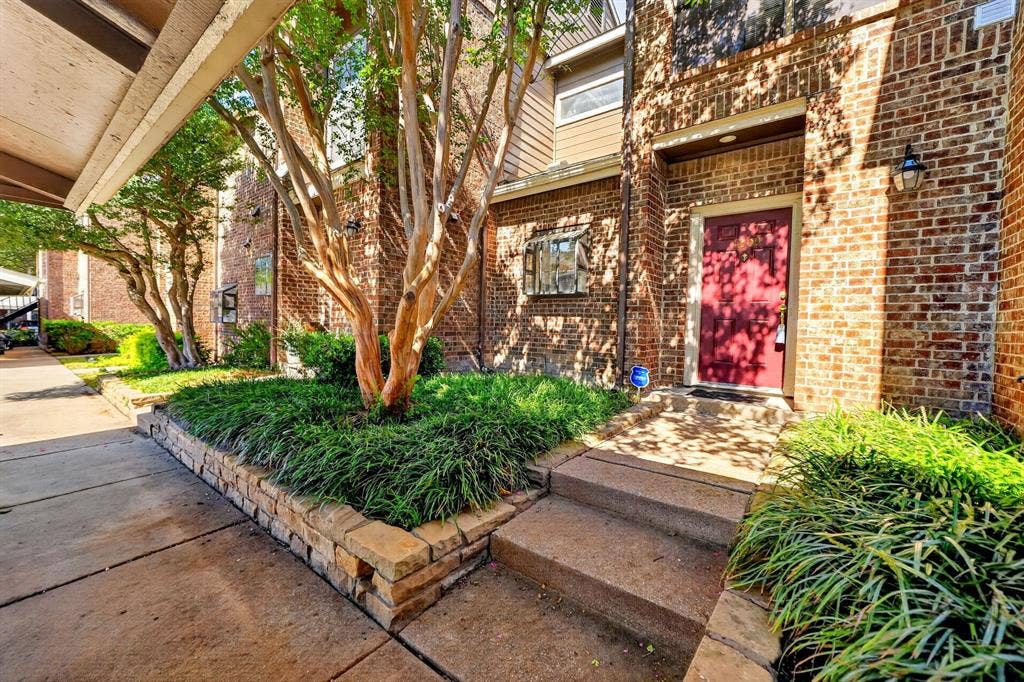 5859 Frankford Road, #1209, Dallas, TX 75252 Brick facade exterior featuring a solid red entry door, stacked stone retaining wall, mature crepe myrtle tree, and concrete walkway
