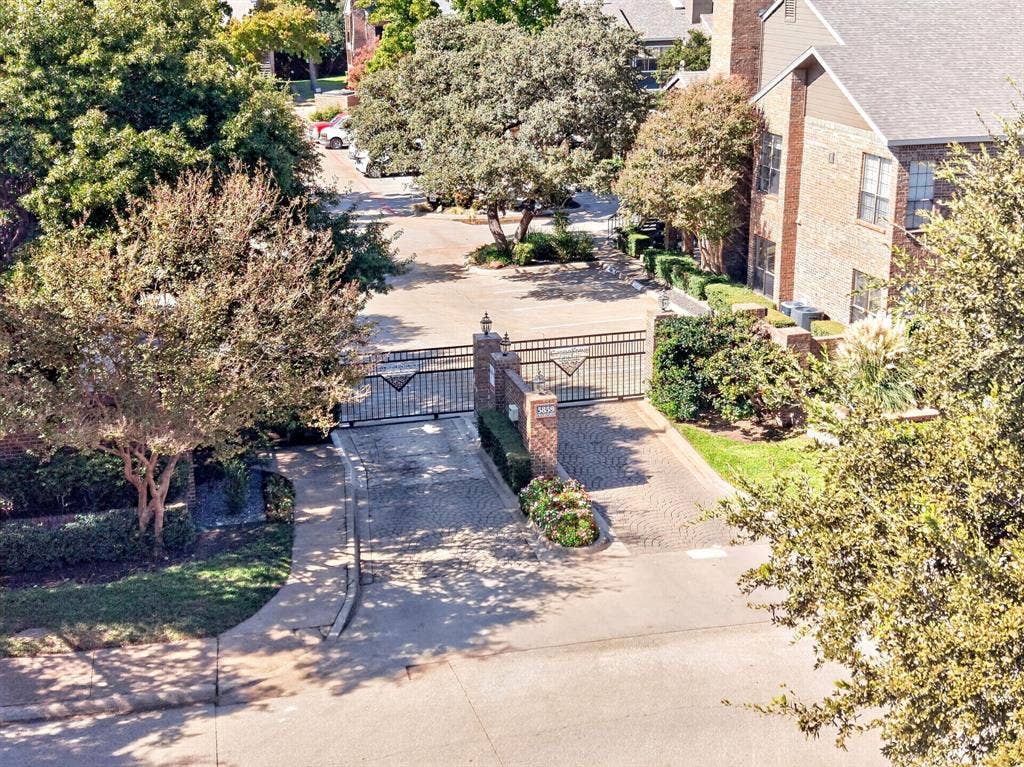 5859 Frankford Road, #1209, Dallas, TX 75252 Gated entrance featuring decorative iron fencing, brick-pillar accents, stone-paver driveway, and mature landscaping