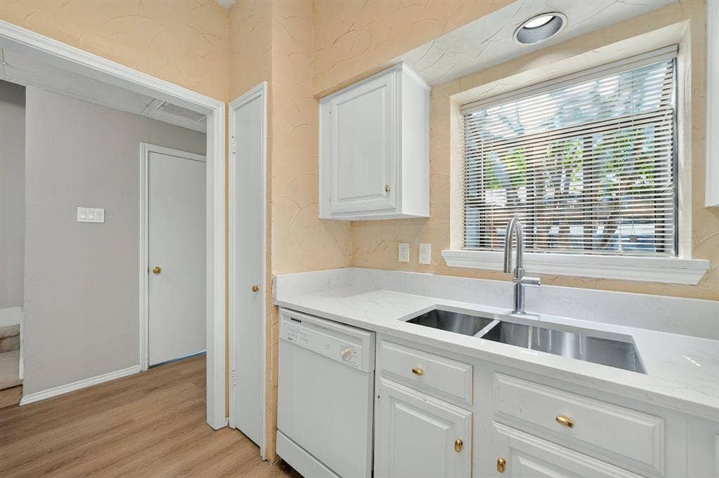 5859 Frankford Road, #1209, Dallas, TX 75252 Kitchen featuring white cabinetry, solid-surface countertops, dual-basin stainless steel sink with high-arc faucet, integrated dishwasher, and wood-finish flooring