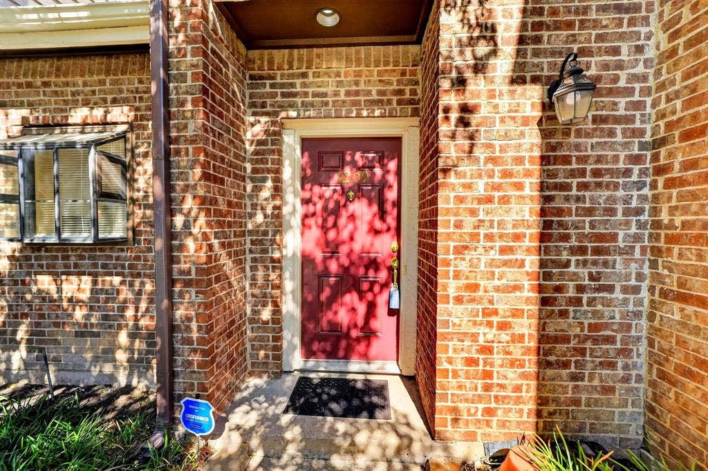 5859 Frankford Road, #1209, Dallas, TX 75252 Exterior entrance featuring full-height brick masonry, a paneled door with brass-finish hardware, and a wall-mounted lantern-style fixture