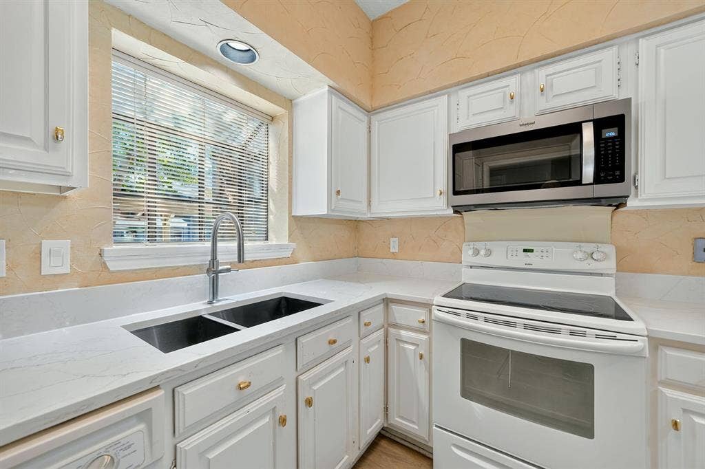 5859 Frankford Road, #1209, Dallas, TX 75252 Kitchen featuring white shaker-style cabinetry, quartz countertops, dual-basin undermount sink with high-arc faucet, and stainless steel over-the-range microwave