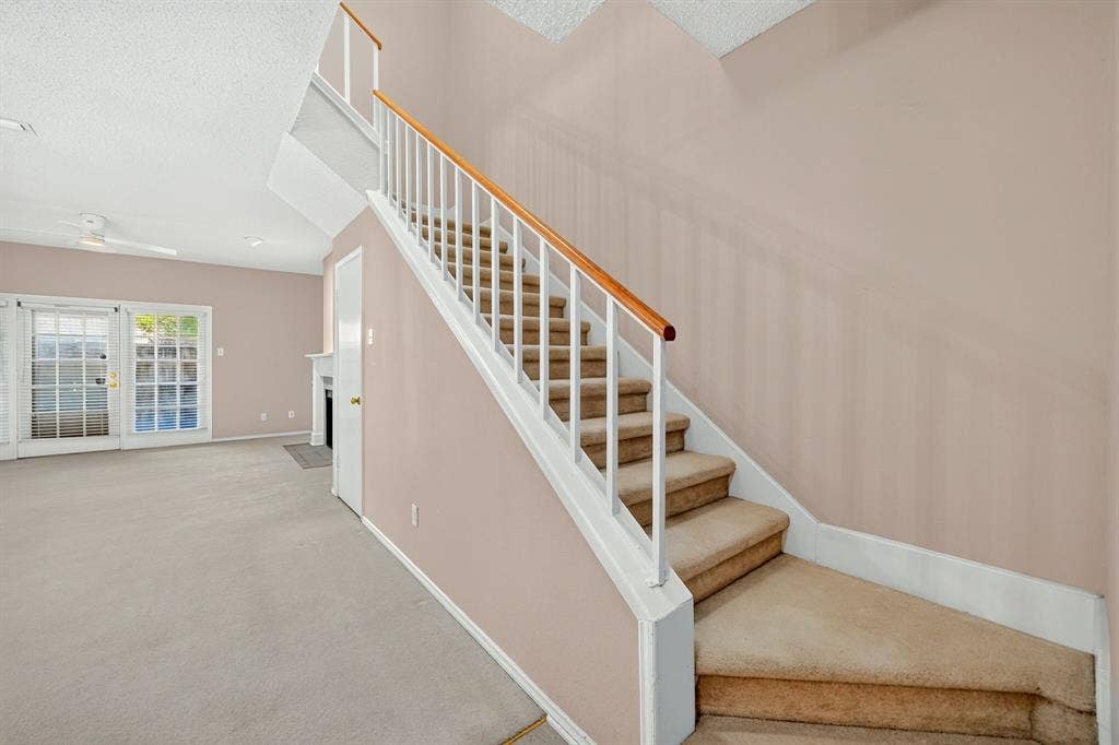 5859 Frankford Road, #1209, Dallas, TX 75252 Staircase with white railing and wood-tone handrail, carpeted steps, glass-paneled exterior door, and fireplace surround