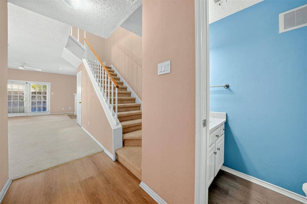 5859 Frankford Road, #1209, Dallas, TX 75252 Staircase with white railing and wood-finish handrail, carpeted steps, wood-finish flooring, white vanity with stone-top surface, and dual French doors