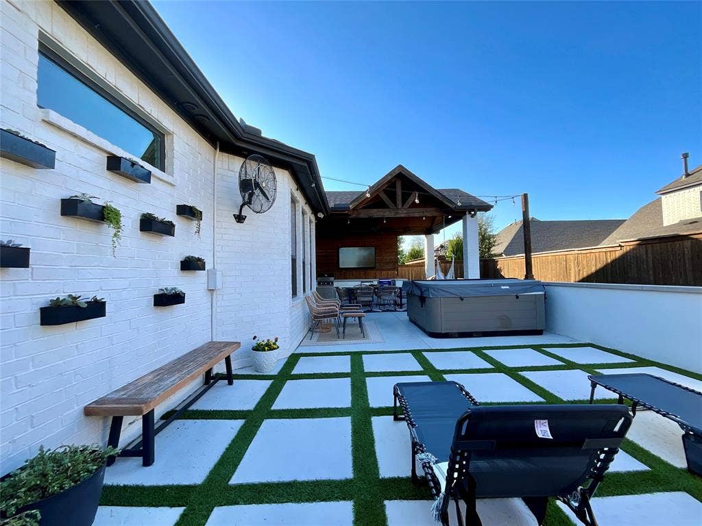 2712 War Admiral Street, Celina, TX 75009 Patio area featuring a painted brick exterior, wall-mounted planters, geometric concrete pavers with grass inlay, and a covered timber-framed structure