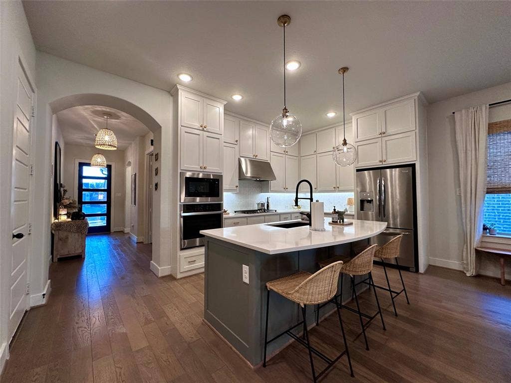 2712 War Admiral Street, Celina, TX 75009 Kitchen featuring white ceiling-height cabinetry, quartz countertops, a contrasting central island, stainless steel built-in appliances, and wood-finish flooring