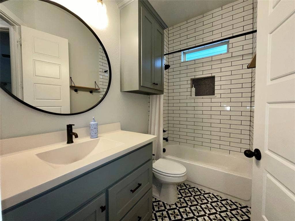 2712 War Admiral Street, Celina, TX 75009 Bathroom featuring a grey vanity with a solid surface countertop, matte black hardware, oval mirror, white subway tile shower surround with a built-in niche, and patterned floor tile
