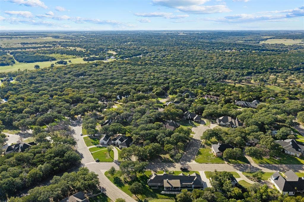 1027 Dominion Oaks Drive, China Spring, TX 76633 Aerial perspective featuring a residential setting with paved roadways, concrete sidewalks, multi-gabled rooflines, and mature woodland canopy