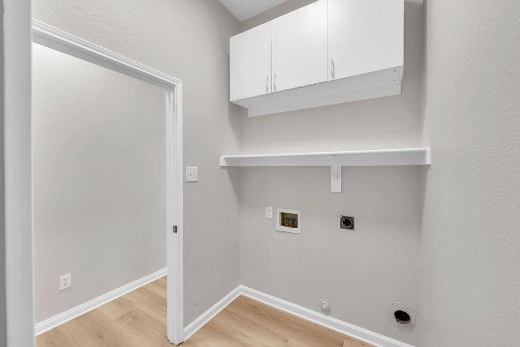 12109 Biloxi Drive, Frisco, TX 75035 Utility area featuring wood-finish flooring, white wall-mounted cabinetry, a fixed open shelf, and dedicated water and electrical hookups