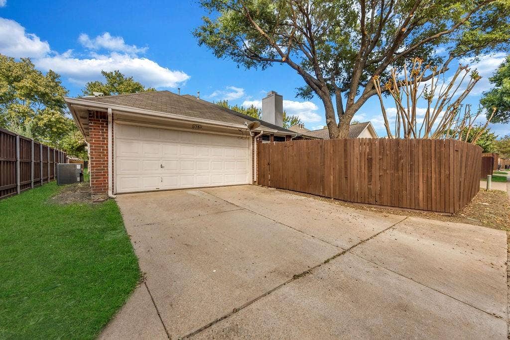 12109 Biloxi Drive, Frisco, TX 75035 Attached two-car garage with brick siding, concrete driveway, and wooden privacy fencing