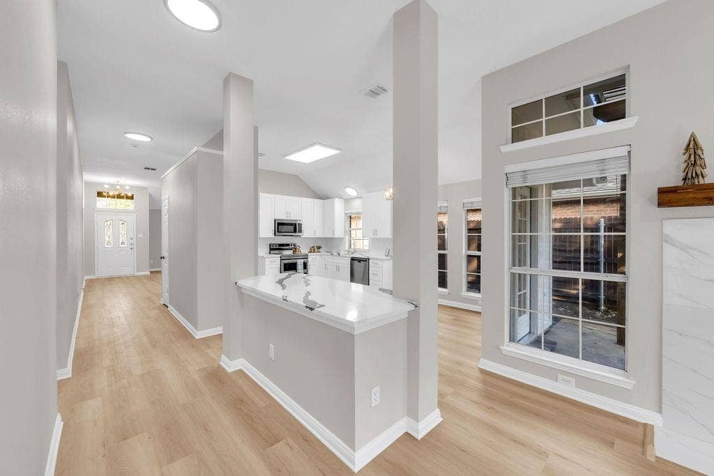 12109 Biloxi Drive, Frisco, TX 75035 Open concept interior featuring light-toned wood-finish flooring, a kitchen island with a stone-surfaced countertop, vaulted ceilings, and large windows with transom panels