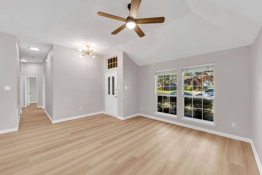12109 Biloxi Drive, Frisco, TX 75035 Vaulted ceiling featuring a central wood-finish blade ceiling fan, light-toned wood-finish flooring, dual windows with grid inserts, and a white entry door with a glass inlay and transom window