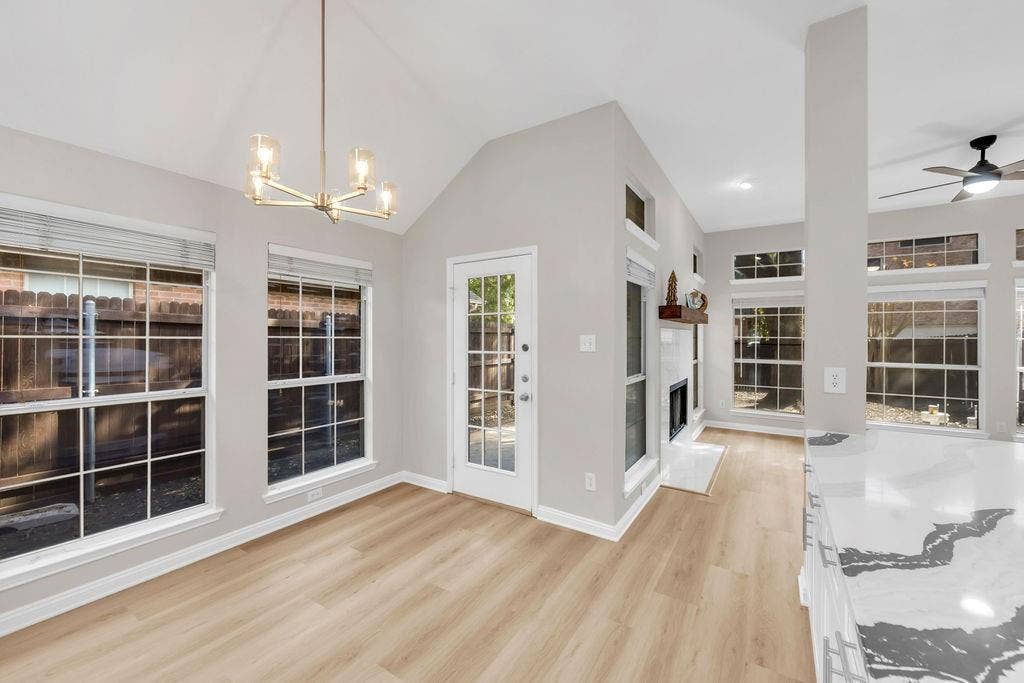 12109 Biloxi Drive, Frisco, TX 75035 Vaulted ceiling featuring a modern metal chandelier, wood-finish flooring, floor-to-ceiling windows, and a built-in fireplace with a stone surround and timber mantel