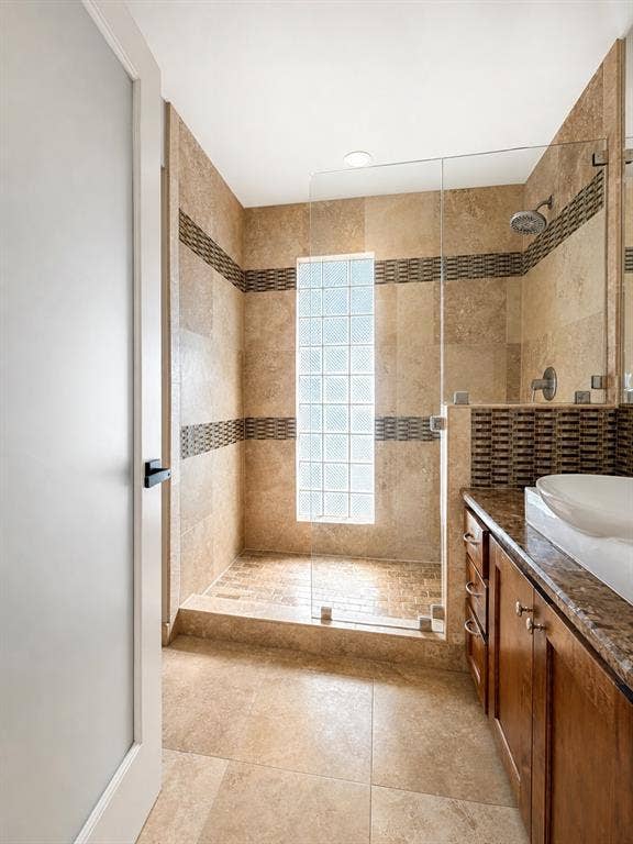 3210 Cortez Court W, Irving, TX 75062 Walk-in shower with glass-block window, stone-tiled walls, glass door enclosure, and wood-finish vanity with a vessel sink and stone countertop