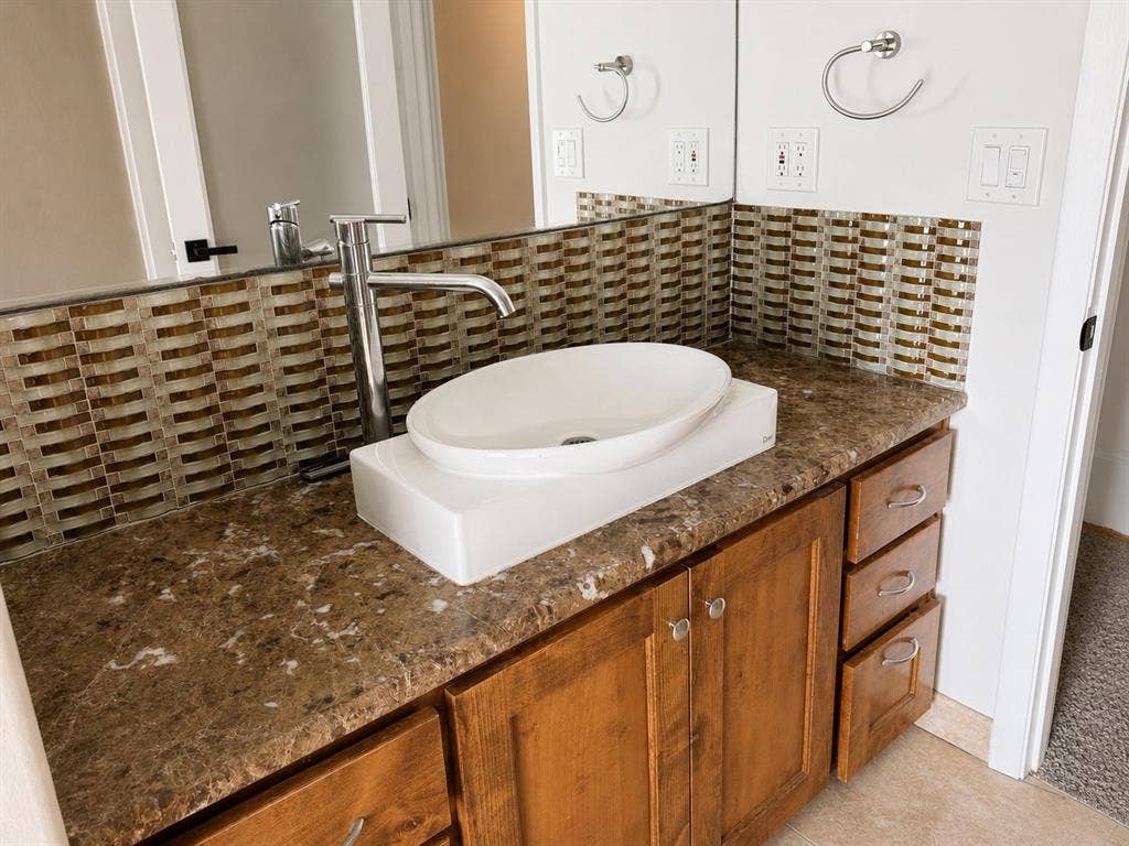 3210 Cortez Court W, Irving, TX 75062 Bathroom vanity featuring a vessel sink, tall metal faucet, stone-finish countertop, wood cabinetry, and a glass tile backsplash