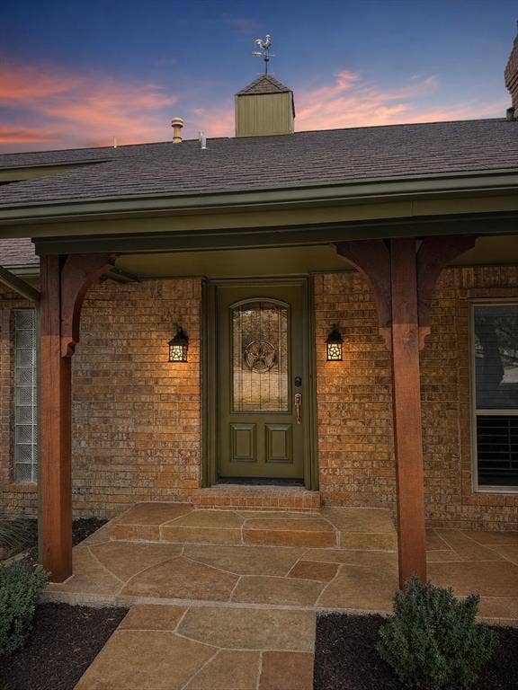 3210 Cortez Court W, Irving, TX 75062 Brick facade entry featuring a flagstone porch, decorative wood support posts, a glass-inset door, and a roof-mounted weathervane