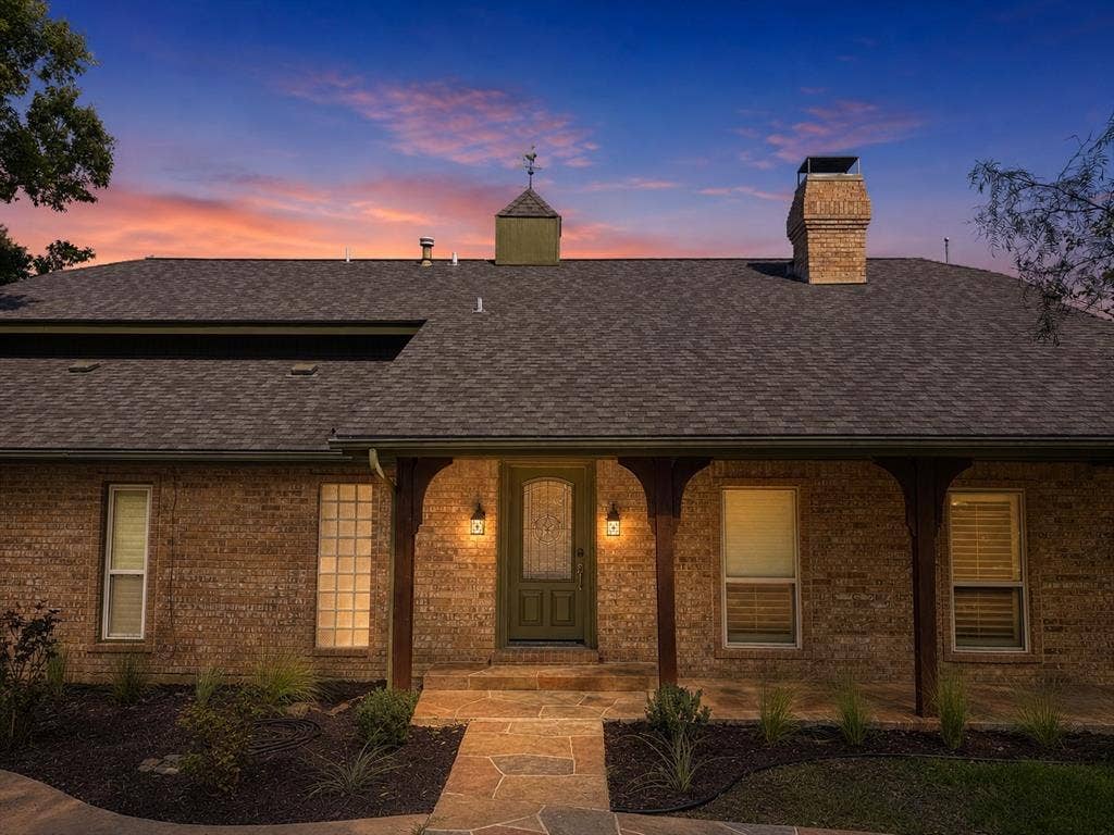 3210 Cortez Court W, Irving, TX 75062 Brick exterior featuring a covered entryway with wood-post supports, a stone-paved walkway, a masonry chimney, and a decorative cupola